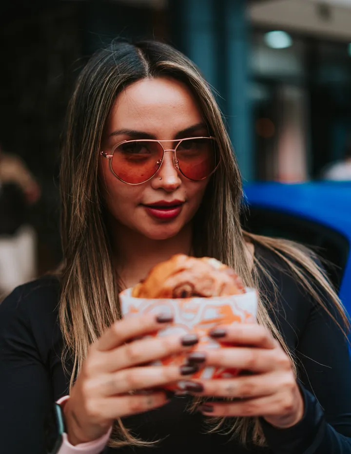 Chica con lentes y su burger junto al coche